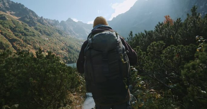 Male hiker backpacker walking stone trail to beautiful mountain lake overlooking incredible highlands landscape during sunny day. Adventure travel explorer in Tatra park, Morskie Oko lake