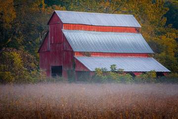Red barn in early morning hours surrounded by fog