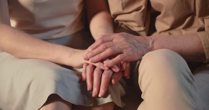 LOVE, SUPPORT AND CARE. Close-up young woman holding wrinkled hands of old senior retired granny supporting and caring.