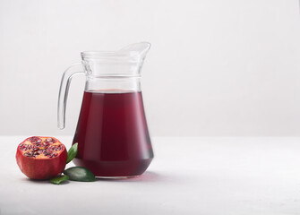 Jug of pomegranate juice with pieces of pomegranate fruits on a white background