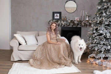 beautiful woman with dog samoyed is sitting in sofa near christmas tree, new year