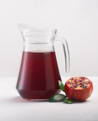 Jug of pomegranate juice with pieces of pomegranate fruits on a white background, close up