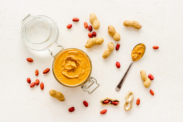 Creamy peanut butter in glass jar with nuts, top view