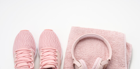 pair of pink textile sneakers, wireless headphones and a textile pink towel on a white background