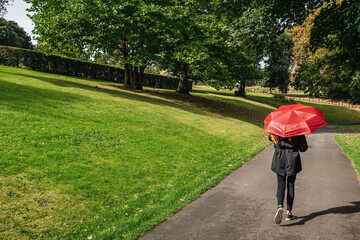 Teenager girl with red umbrella in a park, Autumn fall season concept. Sun and rain weather. Copy space.