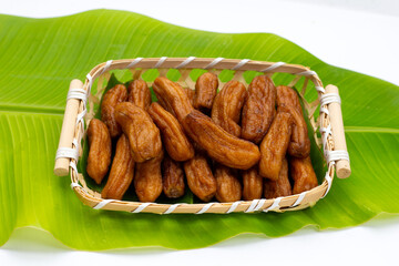 Sun-dried bananas in bamboo basket on banana leaf on white background.