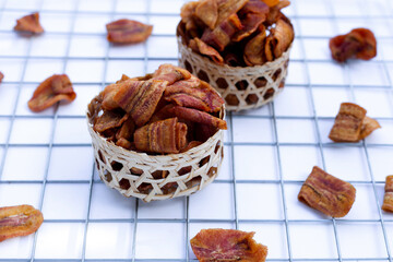 Banana slice chips in bamboo basket on white background.