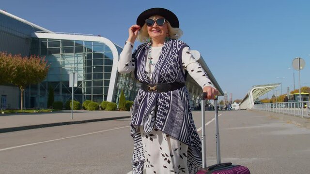 Lovely stylish mature retired grandmother businesswoman walking with luggage suitcase bag to airport hall or railway station for boarding. Travel, vacation, journey, trip. Senior pensioner woman