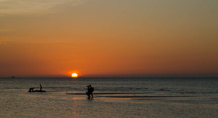 Fototapeta premium Tourists walking at sunset in the middle of the sea at low tide on this paradisiacal island called Holbox, located in Mexico.