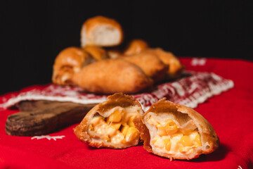 Close-up of a corn empanada cut in half with empanadas and small breads on the bottom.