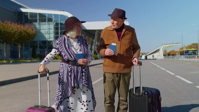Senior couple happy pensioner tourists grandmother grandfather stay with luggage suitcases, tickets, passports from international airport hall or railway station. Travel, vacation, journey, trip