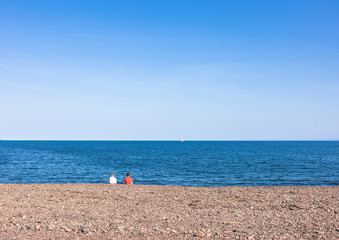 Fototapeta na wymiar Young couple sitting on the beach at seascape view