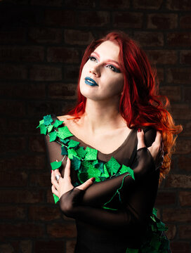 poison ivy comics character cosplay. Halloween costume. young sexy woman in a vine, leaves and poison ivy costume posing as a superhero against brick wall background. female with curly red hair