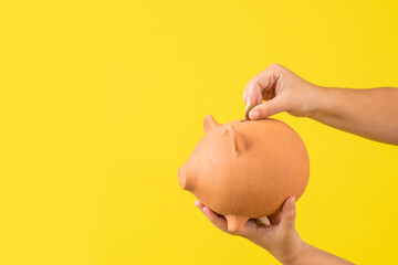 horizontal de las manos de una mujer sosteniendo una alcancía de un cerdo con dinero en fondo amarillo - obrazy, fototapety, plakaty