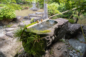 Large stone water basin with bamboo pipe. Japanese garden motif.