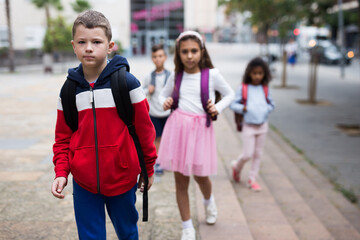 Obraz premium Portrait of cute tween boy with backpack walking with other schoolchildren to school campus after lessons on warm fall day.