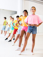 Obraz premium Cute preteen girl with group of children lined up one after another practicing ballet moves during choreography class in studio.