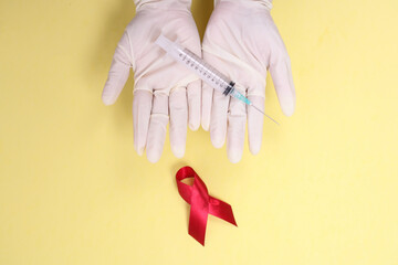 red ribbon with medical gloves and syringe against HIV isolated on yellow background