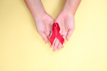 red ribbon in the palm of the hand against HIV isolated on yellow background