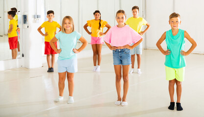 Young boys and girls standing with hands on their waists in dance studio.