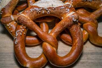 Brown baked pretzel with many other pretzel in the background on a wooden table