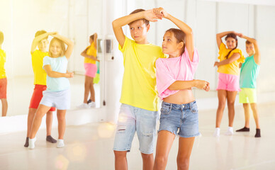 Portrait of positive tweenagers practicing slow ballroom dances in pairs in choreographic studio.