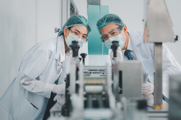 Both male and female Asian scientists are outfitted with protective gear. Examining the factory's machinery and materials used in the mask-making process. Covid 19 is a piece of preventive equipment.