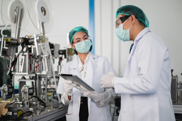 Both male and female Asian scientists are outfitted with protective gear. Examining the factory's machinery and materials used in the mask-making process. Covid 19 is a piece of preventive equipment.