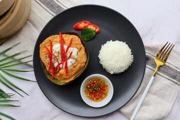 Steamed fish curry in banana leaf cups served with white rice and spicy fish sauce - Famous Thai food called Hor Mok or fish Amok at top view on marble table