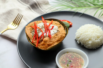 Steamed fish curry in banana leaf cups served with white rice and spicy fish sauce - Famous Thai food called Hor Mok or fish Amok at close up view