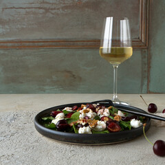a plate of salad with arugula, mozzarella and cherries and a glass of white wine on the table
