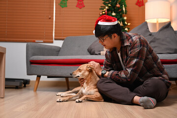 Man in Santa hat playing with his dog in living room.