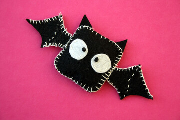 A black bat sewn from felt on a pink background. A toy for Halloween.