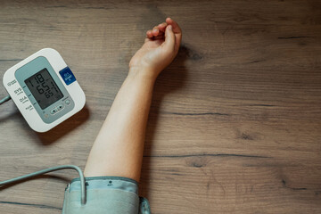 Woman's hand and automatic tonometer on wooden table. On the screen of the device lowered blood...