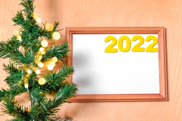 the numbers 2022 in a wooden frame on a wooden background next to the Christmas tree