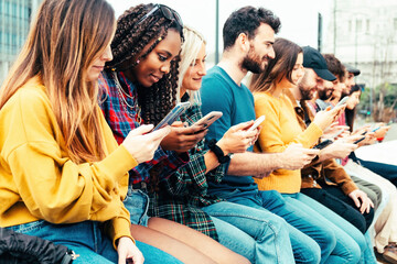 Gruppo di ragazzi multietnico utilizza lo smartphone sedendo all'aperto.