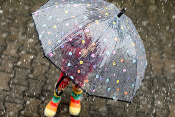 Little toddler girl playing with big umbrella on rainy day. Happy positive child running through...