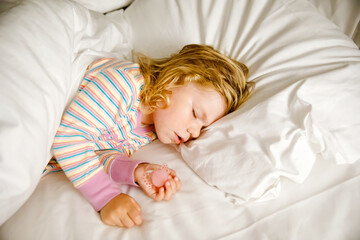 Cute little toddler girl sleeping in big bed of parents. Adorable baby child dreaming in hotel bed on family vacations or at home.
