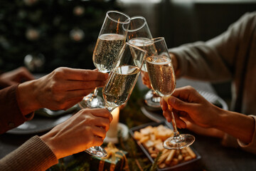Close up of four people enjoying Christmas dinner together and toasting with champagne glasses...