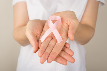 Photo of girl in white t-shirt holding pastel pink ribbon in palms symbol of breast cancer...