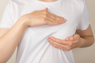 Photo of woman in white t-shirt self examining her breasts on isolated grey background