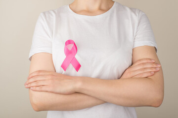 Photo of girl with crossed arms in white t-shirt with pink ribbon symbol of breast cancer awareness on isolated grey background