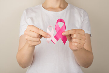 Photo of young woman in white t-shirt demonstrating two pink ribbons symbol of breast cancer awareness on isolated grey background