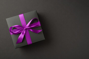 Overhead photo of black giftbox with violet ribbon wrapped as bow isolated on the black background