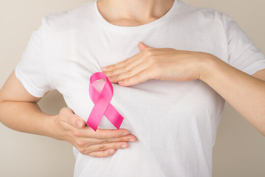 Photo of woman in white t-shirt with pink ribbon self examining her breasts on isolated grey background