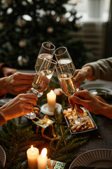 Vertical close up of four people enjoying Christmas dinner together and toasting with champagne...