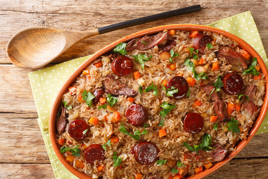 Portuguese duck rice arroz de pato cooked with red wine, onion, carrot and chorizo close up in the baking dish on the wooden table. Horizontal top view from above