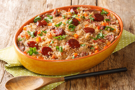 Authentic Arroz de pato duck rice is a traditional recipe from Portugal cooked with red wine, onion, carrot and chorizo close up in the baking dish on the wooden table. Horizontal