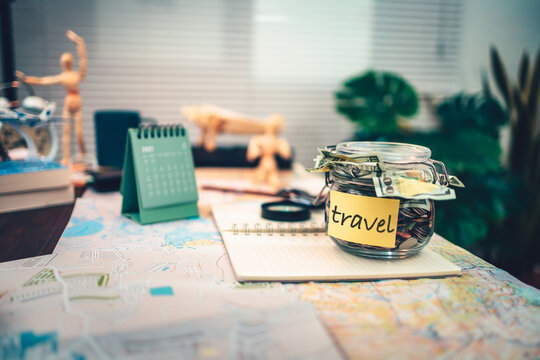 Saving money in glass jar for travel, holiday, vocation on dairy and map on the table. Travel budget concept.