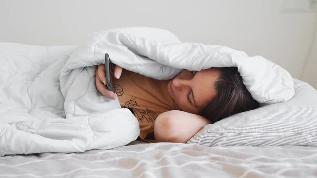 Young woman goes to sleep with teddy bear in her bedroom. Phone addiction, insomnia. Checking social media. Circadian rhuthm.